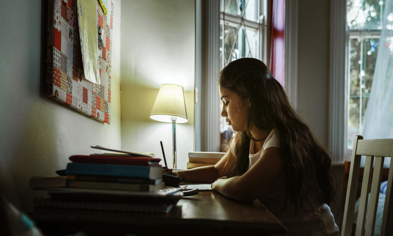 school girl doing homework at desk by desk light