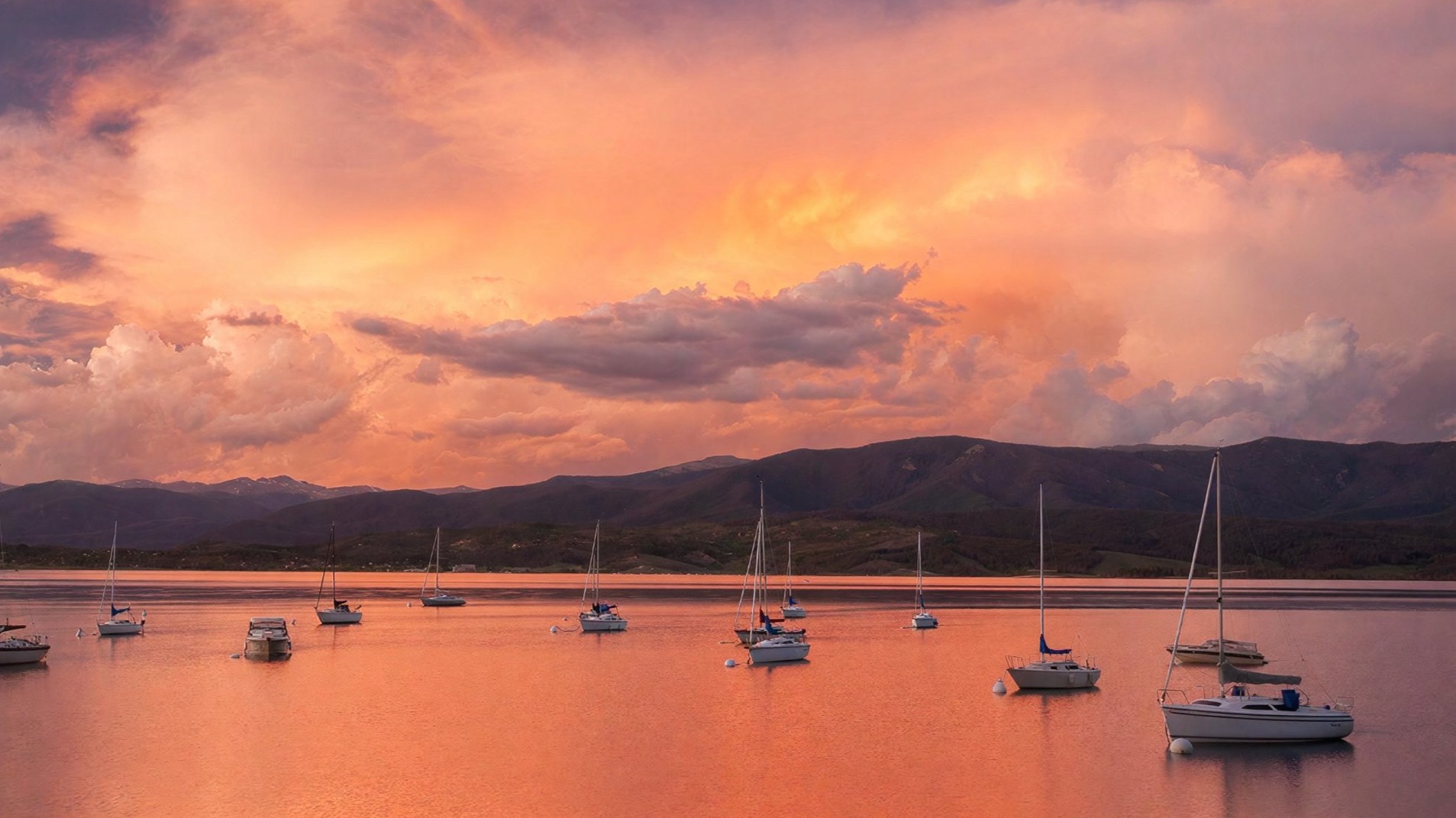 Storm clouds lit orange at sunset over a mountain range.